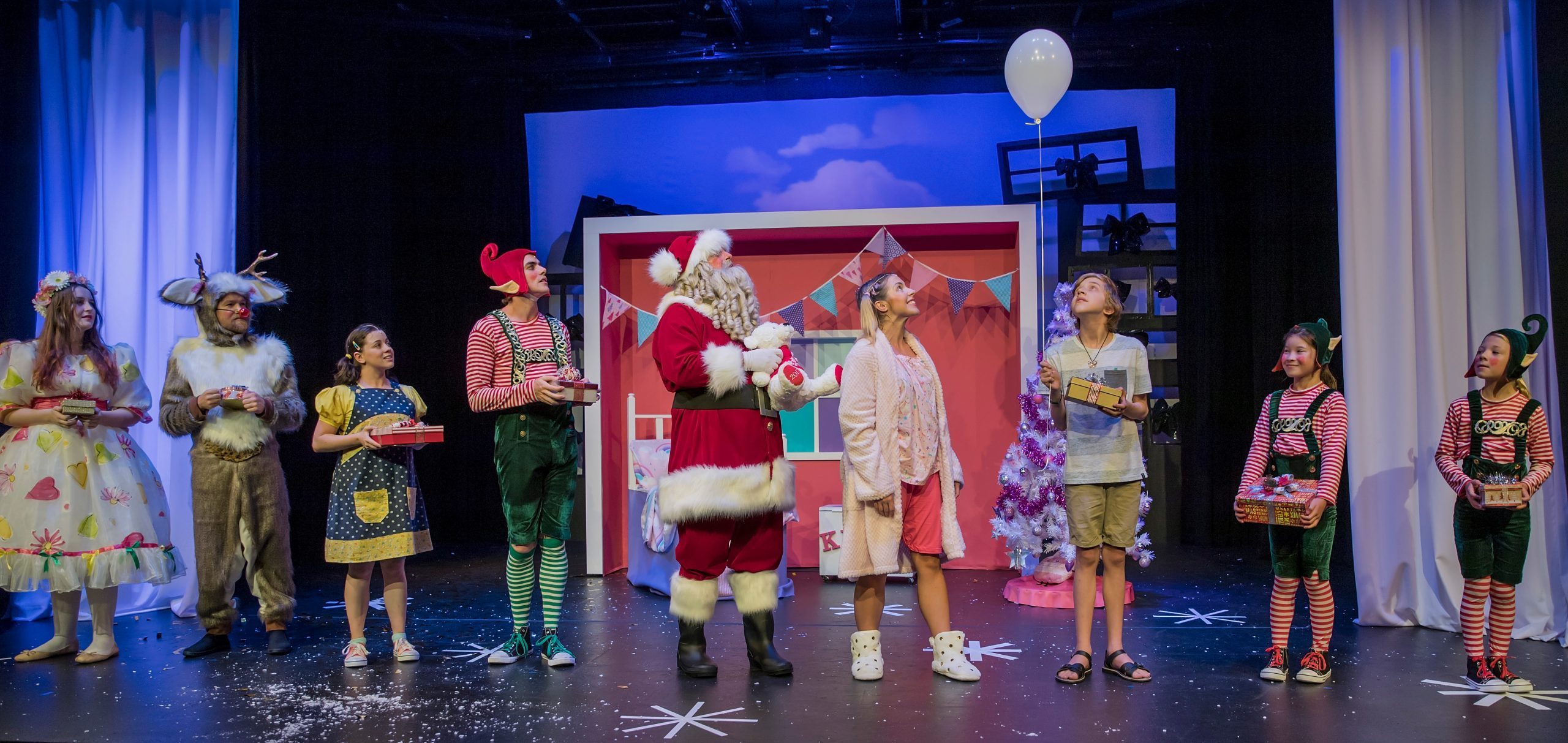 A line of all the Christmas show characters across the front of the stage, gazing up at a white balloon held by a young boy. Behind them is Kelly's pink bedroom.