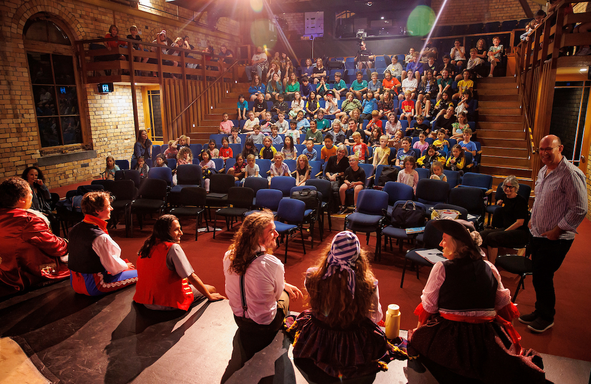 Actors seated on stage and talking to young audience members in the theatre during a performance of The Great Piratical Rumbustification